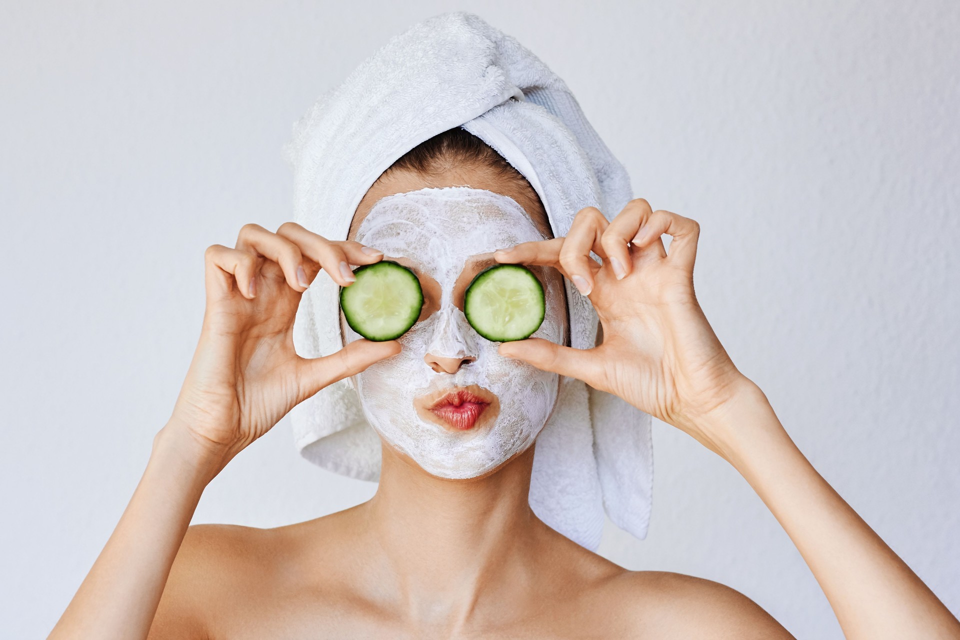 Beautiful young woman with facial mask on her face holding slices of fresh cucumber